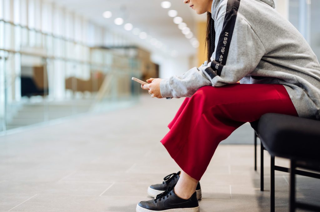 En person sitter på en bänk i korridoren med en telefon i handen.