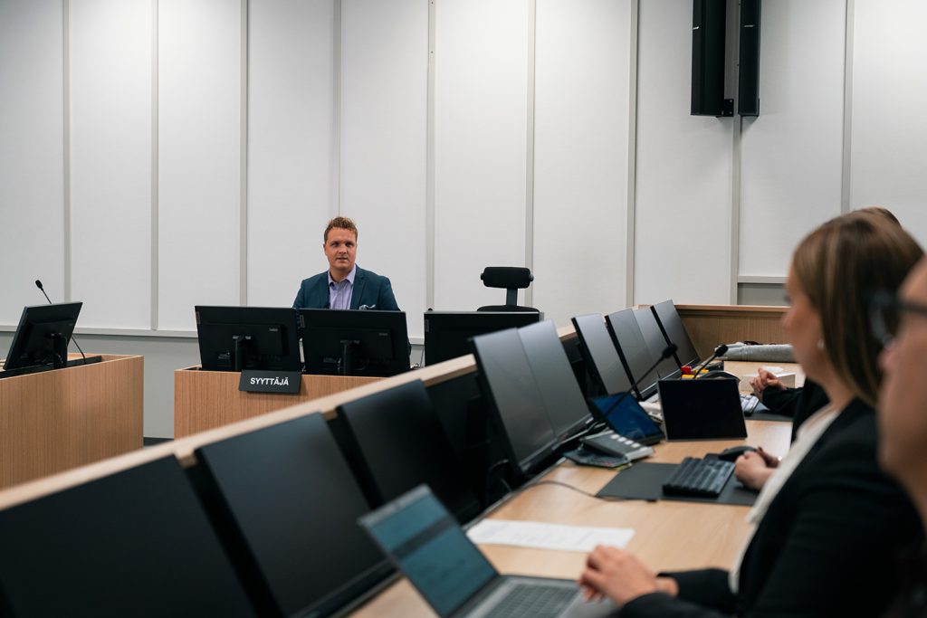 Syyttäjä ja tietokoneiden ääressä istuvia ihmisiä oikeussalissa.